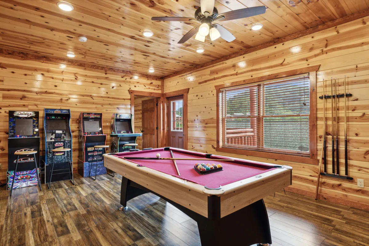 This image features a spacious game room with a pool table and multiple arcade machines nestled against rustic wooden walls. The layout invites socializing, friendly competition, and nostalgic fun.