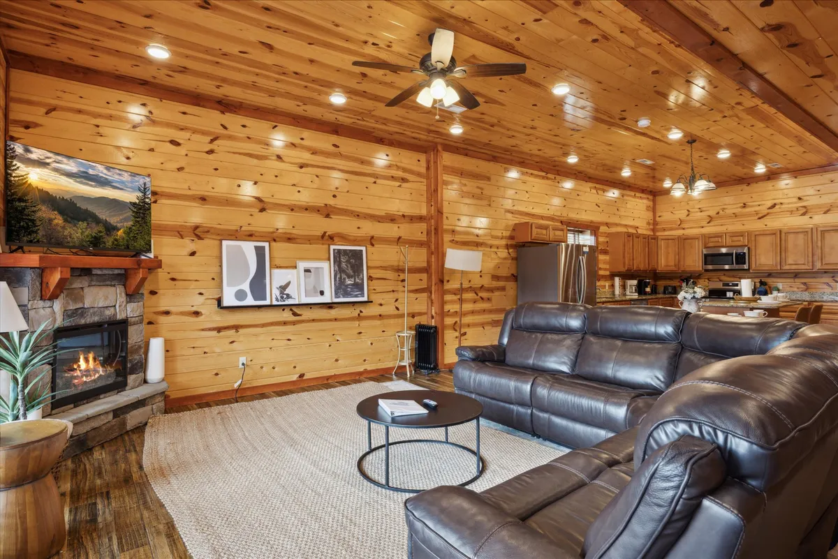 A comfortable living room featuring a plush leather sectional, a striking stone fireplace, large TV, and artwork on the walls. The room exudes warmth and is arranged for relaxing, watching movies, or gathering around the fire with friends and family.