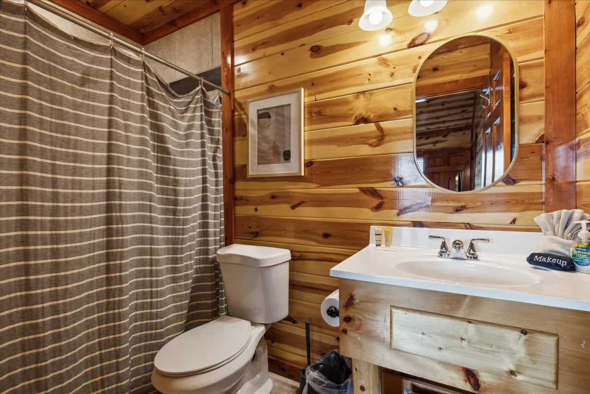 A well-appointed bathroom with wooden paneling, an oval mirror, shower curtain, and a practical vanity with sink. The inviting and warm ambiance suggests comfort and relaxation for personal grooming or unwinding at the end of the day.