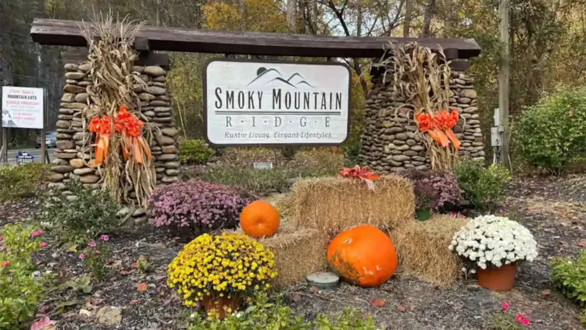 A festive exterior setting with rustic signage, pumpkins, hay bales, and colorful flowers, evoking the spirit of local autumn festivals and small-town charm.