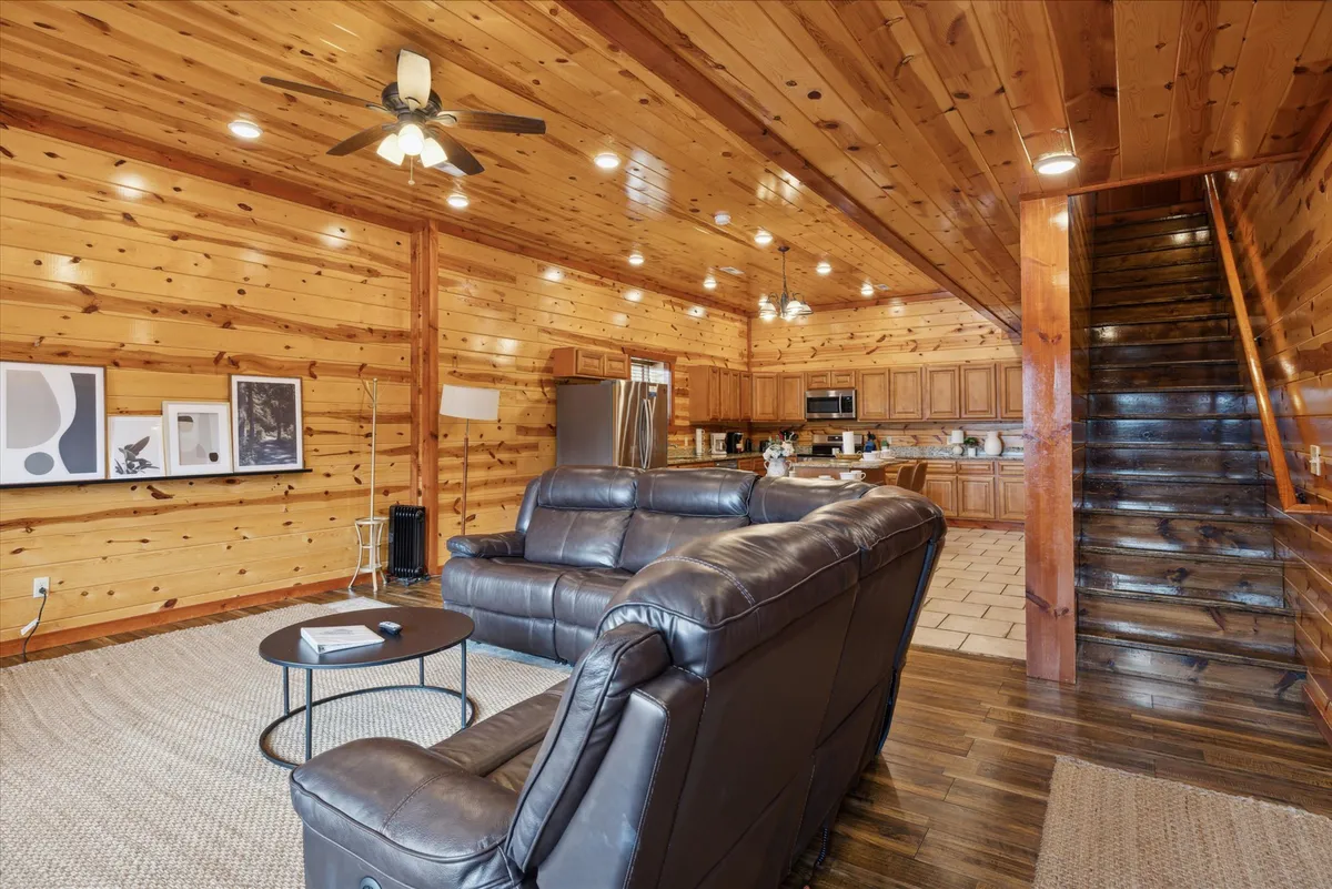 An open-plan interior with a comfortable leather sofa, a warm wooden staircase, and a view into the kitchen area. Artwork adorns the walls, and the scene feels both homey and conducive to both relaxation and entertaining guests.